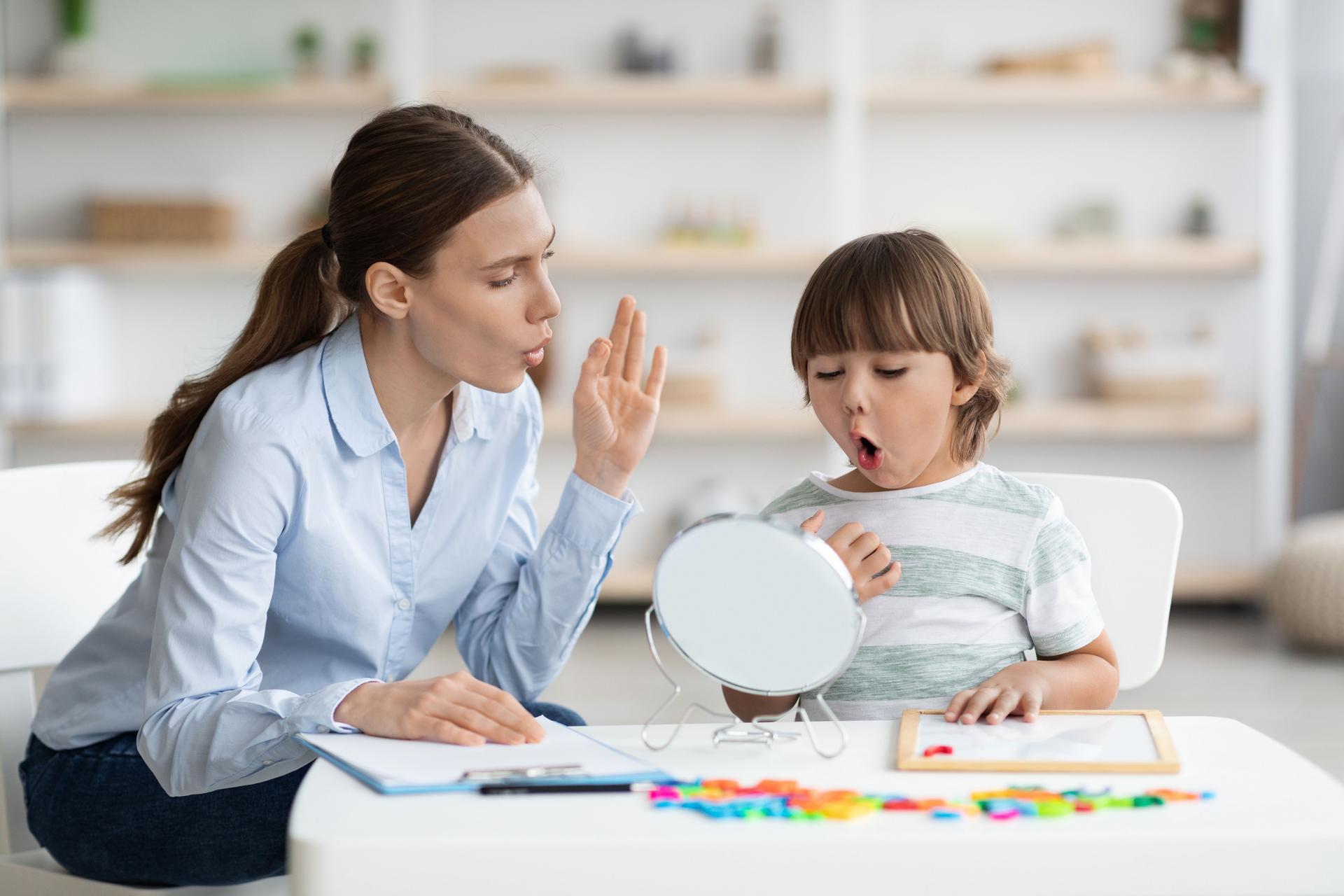 Cute little boy pronouncing sound O looking at mirror, professional woman therapist teaching kid right pronounciation