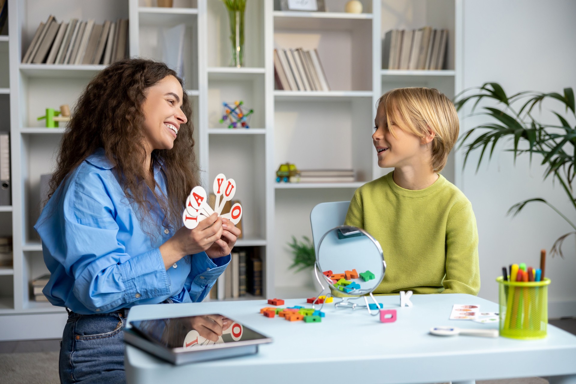 Long-haired speech therapist demonstrating exercises to a blonde boy